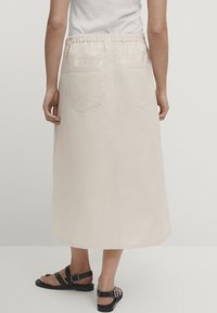Beige bomulds midi-nederdel med elastisk talje, to baglommer og en let udsvinget kant. Glat tekstur og minimalistisk design.