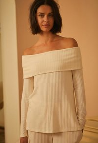 Off-shoulder, geribbelde top in licht beige, met lange mouwen en een relaxte pasvorm; textiel met horizontale lijnen.