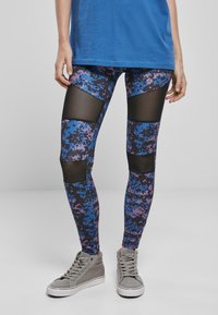 Leggins sadrže plavi, ljubičasti i crni digitalni kamuflažni uzorak s mrežastim panelima na bedrima. Upareni su s sivim visokim tenisicama.
