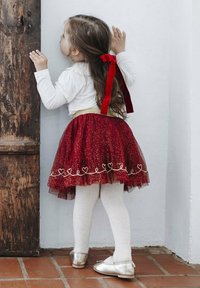 Gonna in tulle rossa scintillante con vita dorata, maglietta bianca a maniche lunghe, collant bianchi e scarpe argentate; capelli legati con un nastro rosso.