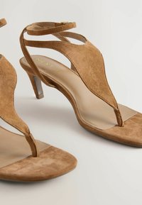 Sandalias de tacón de ante marrón con un diseño de tira en T, punta abierta y correas en el tobillo. Los tacones miden aproximadamente 6.5 centímetros de altura. Forro interior suave.