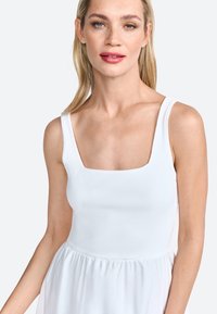 Witte jurk met een fitted ribbenlichaam en een vierkante halslijn, en een vloeiende, geraffineerde rok. Glad textuur met een lichte, luchtige uitstraling.