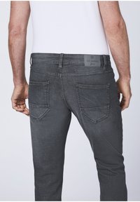 Gray denim jeans featuring a slim fit, five-pocket design, and a label at the waist. The fabric has a slight texture and faded appearance.
