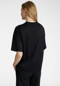 T-shirt nero a maniche corte con vestibilità comoda, realizzato in tessuto morbido. Visto da dietro, presenta un design semplice e senza loghi visibili.