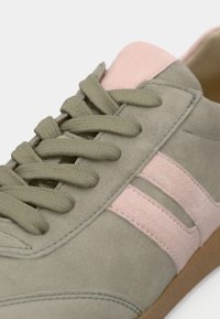 Gros plan d'une basket en daim gris avec des touches roses, des lacets gris épais et une semelle en caoutchouc marron.