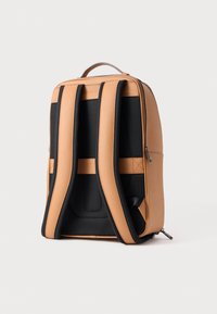 Tans en zwarte rugzak met een gestructureerde afwerking. Voorzien van gevoerde schouderbanden, minimalistisch design en een draaghandvat aan de bovenkant. Ritsvak aan de zijkant.