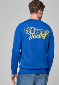 Niebieski sweatshirt z żółtym napisem "Williams Racing" na plecach, z białymi akcentami w paski na ramionach i ściągaczami przy mankietach.