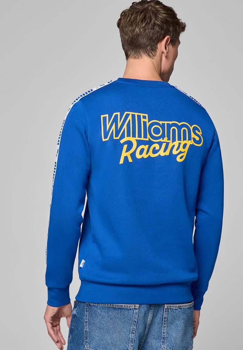 Niebieski sweatshirt z żółtym napisem "Williams Racing" na plecach, z białymi akcentami w paski na ramionach i ściągaczami przy mankietach.