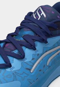 Μπλε αθλητικό παπούτσι με σκούρες μπλε κορδόνια, ασημί λογότυπο στο πλάι και διακοσμητικό πάνω μέρος με διακριτικές γραφικές λεπτομέρειες.