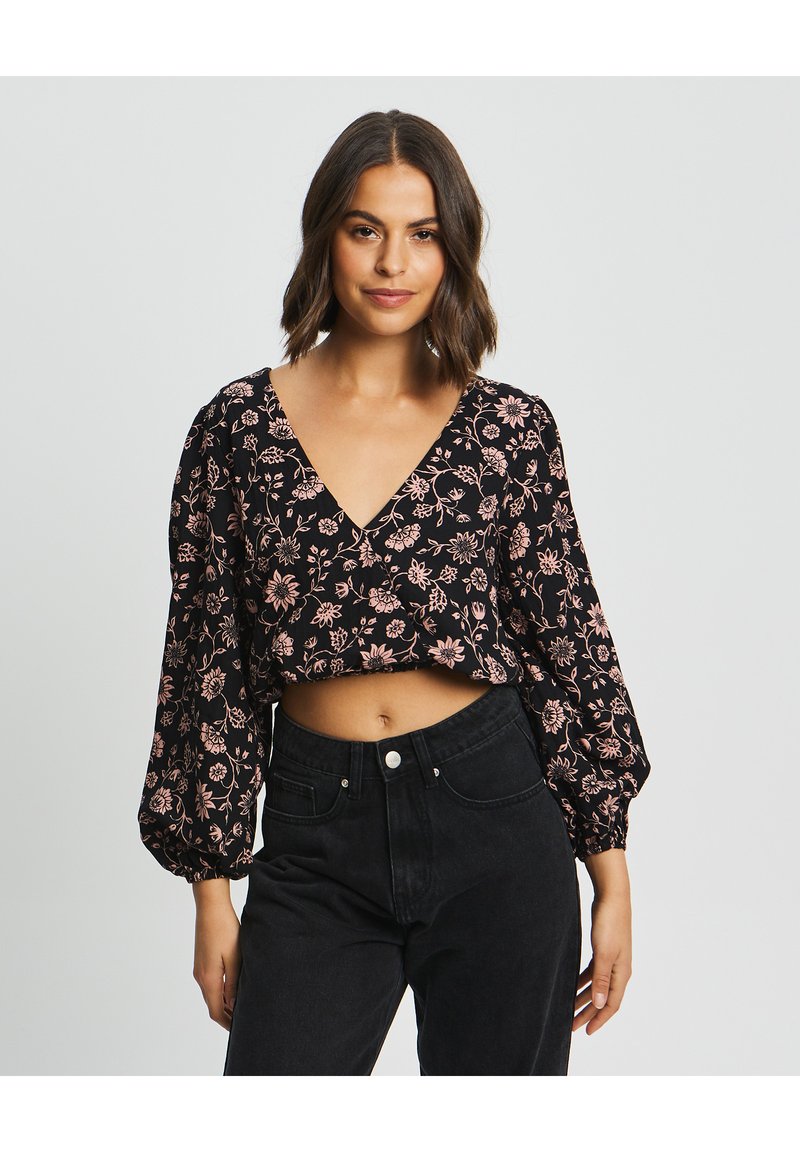 Čierny kvetinový crop top s nafúknutými rukávmi a výstrihom do V, zdobený ružovými kvetinovými vzormi. Skombinovaný s čiernymi džínmi s vysokým pásom.