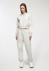 Jasnoszara, krótka bluza z kapturem i zamkiem z przodu, w zestawie z jasnoszarymi spodniami dresowymi z elastycznym pasem i mankietami.