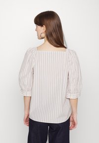 Blusa leve, riscada a creme, com mangas bufantes, decote quadrado e detalhes em botão nos punhos. Linhas verticais em azul-marinho.