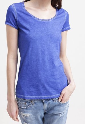 Niebieska, krótka koszulka z krótkim rękawem i okrągłym dekoltem, wykonana z miękkiej, teksturowanej tkaniny. Połączona z przetartymi jeansami.