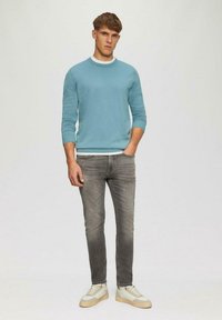 Turquoise gebreide trui met ronde hals, lichtgrijze jeans en beige sneakers. De trui heeft ribbelboorden en een ribbelzoom.