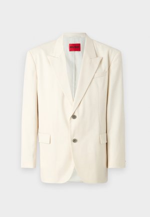 Blazer em beige claro, bem ajustado, com lapelas recortadas, dois botões à frente, um bolso no peito e bolsos laterais, feito de um tecido suave. Etiqueta da marca visível.