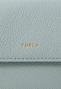 Lichtblauwe leren portemonnee met textuur en gouden "FURLA" branding, met zichtbare stiksels en een gladde afwerking.