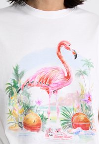 Hvid bomulds T-shirt med et stort pink flamingo-illustration, to orange basketballer og pink sneakers blandt tropiske planter og blomster.