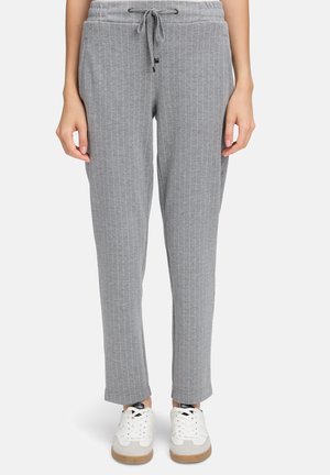 Pantaloni jogger grigi a righe con cintura drawstring, vestibilità slim e gambe affusolate, abbinati a sneakers bianche e una superficie testurizzata.