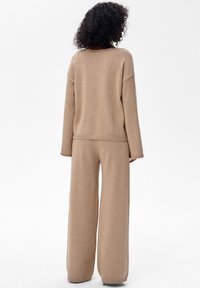 Dwuczęściowy zestaw w beżowym kolorze o miękkim, teksturowanym wykończeniu. Góra ma luźny krój, opuszczone ramiona i ściągacze przy brzegu; spodnie są szerokie.