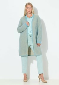 Hellblauer gestrickter Cardi gan mit langen Ärmeln, getragen über einem passenden hellblauen Oberteil und einer passenden Hose. Beige High Heels vervollständigen das Outfit.