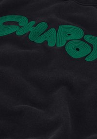 Zwarte stof met verhoogde groene geborduurde tekst die "SNAPO" spelt in vetgedrukte, afgeronde letters.