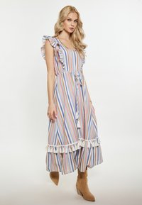 Rochie maxi cu dungi, cu mâneci volănașe, talie cu șnur și margine cu ciucuri albi. Culorile includ albastru, roz și crem. Purtați cu cizme bej.