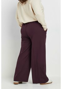 Weite Hosen in einem tiefen Burgunderrot mit weicher Textur. Mit einem elastischen Bund und seitlichen Taschen für zusätzliche Funktionalität.