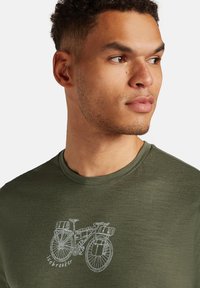 Camiseta verde oliva de tela ligera, con un gráfico en contorno blanco de una bicicleta en la parte frontal y el texto "icebreaker" debajo.