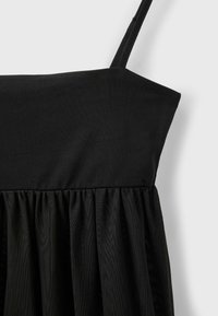 Robe noire sans manches avec un décolleté droit et un tissu transparent froncé sous la poitrine, présentée sur fond blanc.