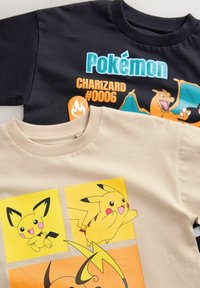 To T-shirts stablet. Den ene er sort med "Pokémon Charizard #0006" tryk; den anden er beige med gule paneler og Pikachu-illustrationer.