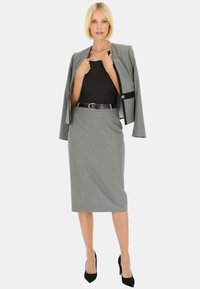 Szary żakiet o dopasowanym kroju z kontrastującym czarnym akcentem, dopasowana ołówkowa spódnica i obcisła czarna bluzka, uzupełnione czarnym paskiem i szpilkami.
