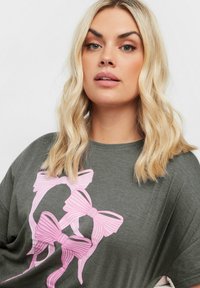 T-shirt in cotone grigio con grandi motivi a fiocco a righe rosa e bianche stampati sulla parte frontale. Vestibilità comoda con maniche corte e scollatura rotonda.