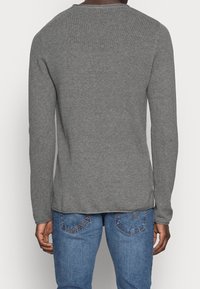 Maglione grigio a maniche lunghe con un design a maglia testurizzata, scollatura rotonda e vestibilità regolare, abbinato a jeans in denim blu.