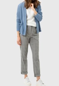 Cardigan côtelé bleu clair, t-shirt blanc, pantalon à carreaux gris en forme de tapered avec cordon de serrage, et baskets blanches. Tenue décontractée avec un fit confortable.