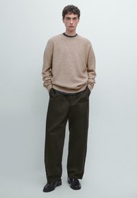 Maglione beige a trama con maniche lunghe, abbinato a pantaloni larghi verde scuro e scarpe nere con lacci. Design semplice e minimalista.