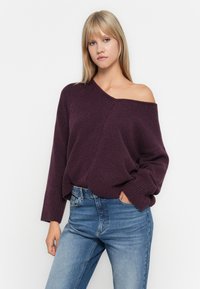 Pull en maille violet avec un design décontracté, des poignets côtelés et une coupe relaxée, assorti à un jean en denim bleu clair.