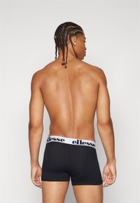 Svarta boxerkalsonger med ett vitt elastiskt midjeband som har varumärket "ellesse" i svart. Slät tyg med en åtsittande design.