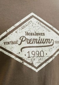 Logo vintage de Jack & Jones Premium con el texto "Calidad Tradición", "Premium" y el año "1990" sobre una tela marrón.