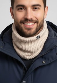 Beige ribbed knit neck gaiter worn over a navy jacket, showcasing textured fabric and a small black logo tag.