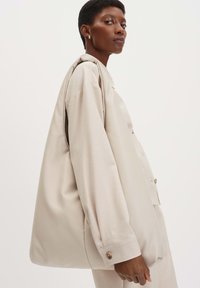Borsa a spalla oversize beige realizzata in materiale liscio, caratterizzata da una forma morbida e cuciture rinforzate. Accentuata da sottili dettagli in metallo.