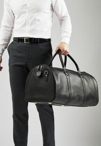 Musta nahkainen duffel-laukku, jossa on pyöristetty muoto, teksturoitu pinta, kaksinkertaiset kahvat ja pieni sivutasku metallilukolla.