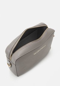 Trousse de maquillage en cuir gris avec une fermeture éclair dorée, présentant une texture douce, une forme structurée et un logo embossé sur le devant.