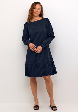 Robe bleu marine avec de longues manches bouffantes, décolleté arrondi et ourlet plissé. Fabriquée en tissu lisse, elle présente un corsage ajusté et une silhouette décontractée.