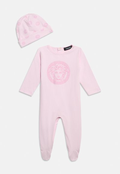 Ροζ μαλακό φορμάκι μωρού με το λογότυπο της Μέδουσας στο στήθος και ταιριαστό καπέλο με κυκλικό μοτίβο, και τα δύο κατασκευασμένα από λείο ύφασμα.