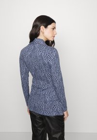 Blusa de manga longa em azul-marinho com um padrão texturizado de bolinhas azul-claro, apresentando um colarinho alto e um design ajustado, feita de material flexível.