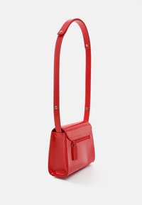 Sac à main en cuir verni rouge avec une forme rectangulaire structurée, doté d'une fermeture plate, d'une poche zippée et d'une longue bandoulière.