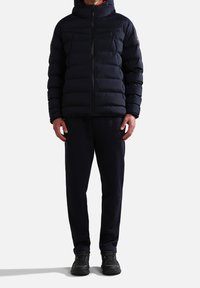 Marineblå pufferjakke med hætte, der har quiltede sektioner og en frontlynlås. Kombinationen består af mørke joggers og sorte sneakers.