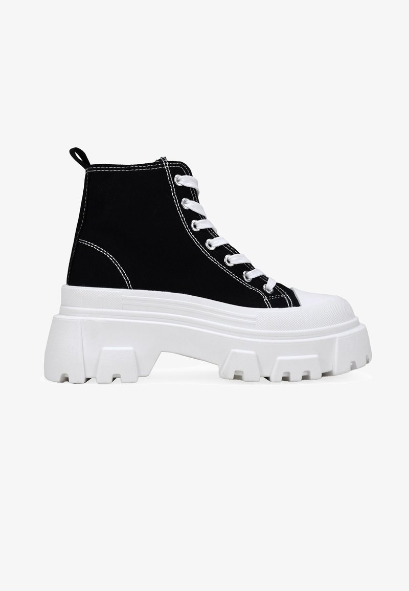 Zapatillas altas de lona negras con cordones blancos, suela blanca gruesa, detalles cosidos y un patrón de tacos distintivo en la suela exterior.