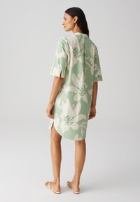 Green floral dress with short sleeves, featuring white and dark green patterns, side slits, and a straight hem. Smooth fabric texture.