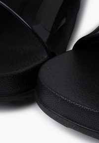 Černé sandály s elegantním a hladkým designem, texturovanou stélkou a lesklým svrškem. Podešve jsou ploché a mírně polstrované.